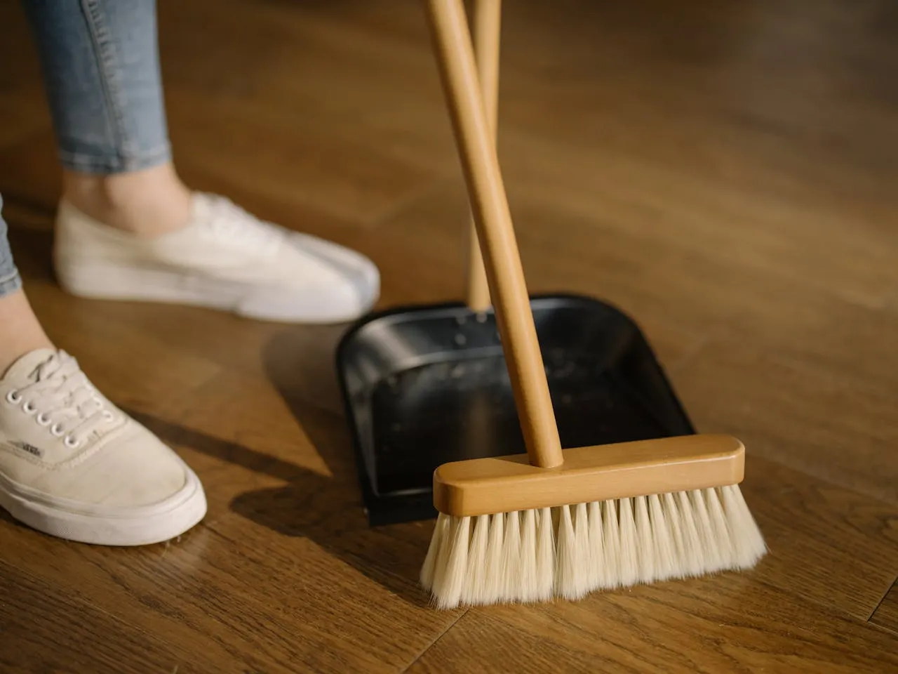 Sweeping a hardwood floor with a broom and dustpan